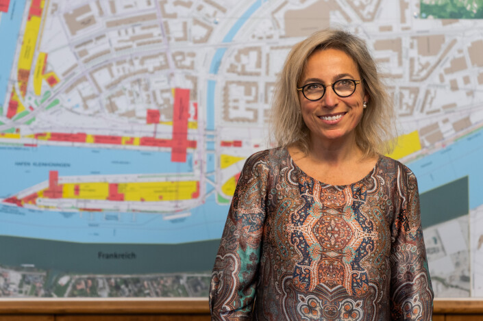 Ein Bild von Marta Martin, Projektmitarbeiterin bei den Schweizerischen Rheinhäfen. Sie steht vor einer Karte, die das Gebiet rund um den Hafen in Basel zeigt.
