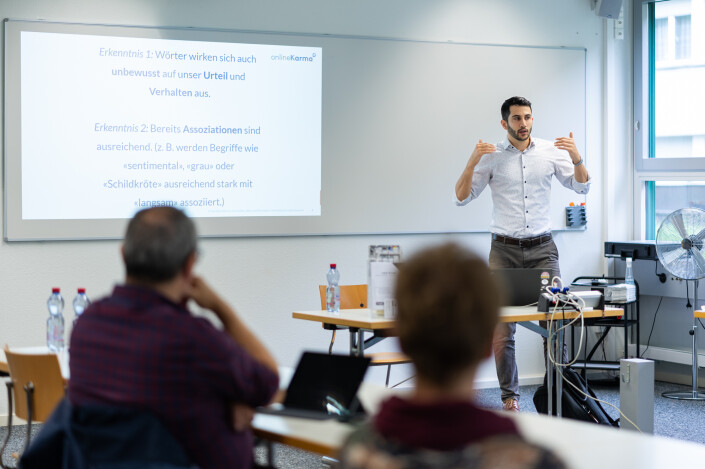 Raphael Guldimann steht vor einer Leinwand und gestikuliert, während er etwas erklärt.